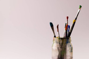 Boya fırçaları ve krem arka planda fotokopi alanı olan kavanozun yakın plan görüntüsü. Resim, sanat ve zanaat konsepti.