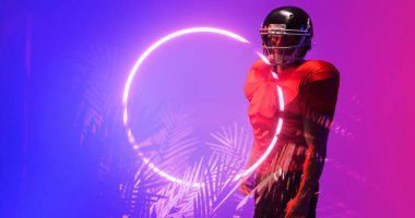 Kırmızı üniformalı ve kasklı Amerikalı futbolcu aydınlanmış çember ve bitkilerin yanında duruyor. Boşluğu kopyala, kompozit, spor, rekabet, illüstrasyon, parlama, doğa, şekil, soyut kavram.