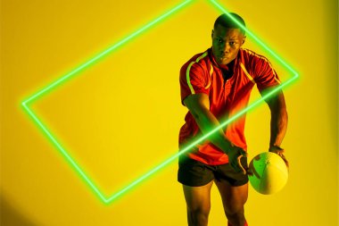 Sarı arka planda oynayan Afrikalı Amerikalı genç rugby oyuncusu üzerinde dikdörtgen neon. Dijital kompozit, spor, rugby, atlet, rekabetçi spor, yetenek, çalma, kopyalama alanı.
