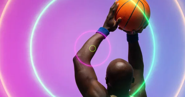 Łysy Afrykański Koszykarz Rzuca Piłką Nad Podświetlanymi Wielobarwnymi Kręgami Kompozyt — Zdjęcie stockowe
