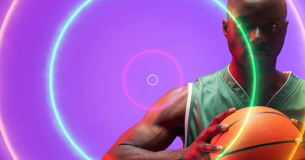 Портрет Серьезного Лысого Африканского Баскетболиста Держащего Мяч Над Разноцветными Кругами — стоковое фото