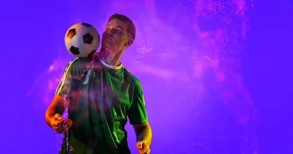 Caucasian soccer player practicing with ball and abstract design over blue background, copy space. Computer graphic, digital composite, soccer, design, athlete, skill, competitive sport.