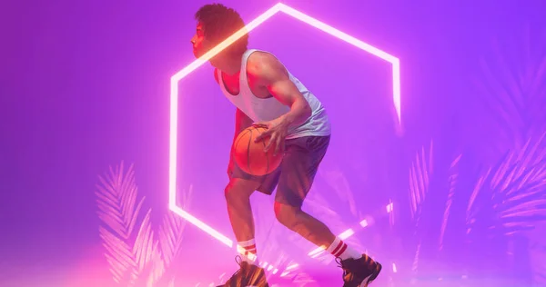 Dwurasowy Koszykarz Dryblujący Piłką Przez Oświetlony Sześciokąt Rośliny Fioletowym Tle — Zdjęcie stockowe