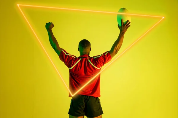 非洲裔美国橄榄球运动员上的三角形霓虹灯 手挽着黄色背景的球 数码合成 橄榄球 运动员 竞技运动 复制空间 — 图库照片