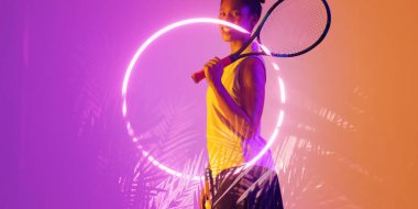 Gülümseyen Afro-Amerikan bayan tenis oyuncusu raketi ile aydınlatılmış çember ve bitkilerin yanında duruyor. Boşluğu kopyala, kompozit, spor, rekabet, şekil, doğa, eşleşme ve soyut kavram.