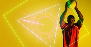 Afrika kökenli Amerikalı oyuncu kollarını kaldırdı ve rugby topunu aydınlatılmış geometrik şekillerin üzerine fırlattı. Boşluğu kopyala, kompozit, spor, rekabet, sarı, çalma, eşleştirme, şekil ve soyut kavram.