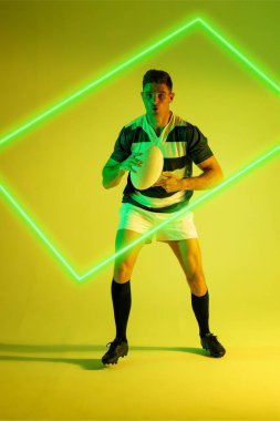 Kafkas erkek rugby oyuncusu, renkli arka planda aydınlatmalı dikdörtgenle top oynuyor. Boşluğu kopyala, kompozit, spor, şekil, rekabet, çalma, eşleşme ve soyut kavram.