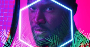 Yanmış altıgen ve bitkilerle tenis raketi ile Afrika kökenli Amerikalı erkek oyuncunun yakın çekimi. Bileşik, pembe, spor, rekabet, şekil, doğa, yüz, portre ve soyut kavram.