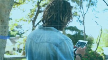 Parkta dijital tablet kullanan bir adam. Dijital olarak üretilen, üç mavi istatistiksel çizginin dijital ekranda artıp azalmasıyla.