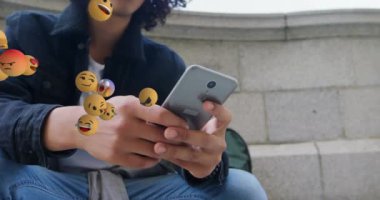 Çift ırklı, kıvırcık saçlı, akıllı telefon kullanan bir adamın üzerinde birden fazla yüzen emoji animasyonu. Dijital bileşik, çoklu pozlama, tepki, sosyal medya, soyut ve teknoloji kavramı.