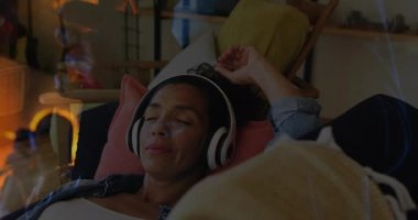 Animation of sunset landscape over biracial woman listening to music with headphones on. Music, arts and leisure time concept digitally generated video.