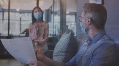 Animation of network of connections over diverse business people wearing face masks at office. Global business, connections and pandemic concept digitally generated video.