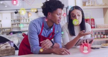 Animation of media icons over diverse shop assistant and customer talking. Global business and digital interface concept digitally generated video.