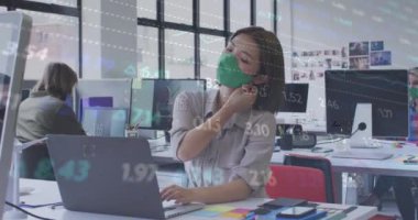 Animation of changing numbers and heart rhythm over asian woman removing mask and smiling in office. Digital composite, multiple exposure, digits, growth, business, safety and technology concept.
