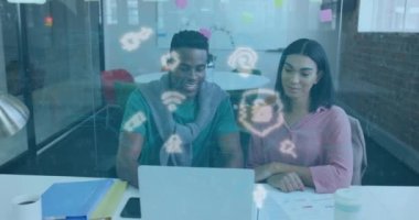Animation of multiple icons over multiracial coworkers discussing reports on laptop in office. Digital composite, multiple exposure, protection, security, teamwork, communication and technology.