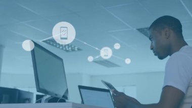 Animation of connected icons over low angle view of african american man using technology in office. Digital composite, multiple exposure, communication, business and abstract concept.