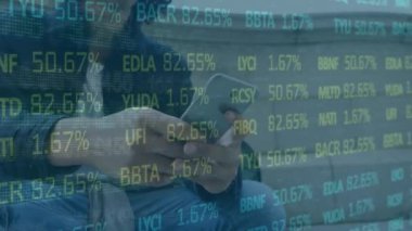 Animation of trading board over biracial man using smartphone in outdoors. Digital composite, multiple exposure, business, stock market, abstract and technology concept.