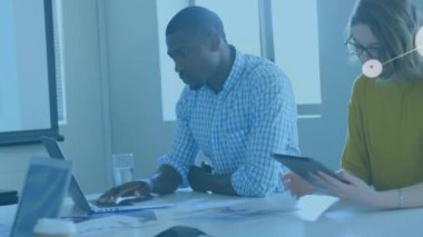 Animation of connected icons over diverse coworkers working on laptop and digital tablet in office. Digital composite, multiple exposure, teamwork, communication, abstract and technology concept.