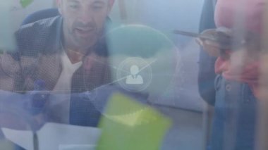 Animation of globe, connected icons, dense clouds on diverse coworkers discussing reports in office. Digital composite, multiple exposure, globalization, communication, abstract, technology concept.