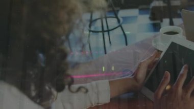 Animation of financial data processing over rear view of woman using digital tablet at a cafe. Global finance and business technology concept