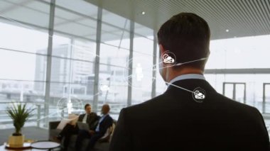 Animation of connected icons with lines over rear view of businessman walking in office. Digital composite, multiple exposure, communication,, cloud computing, abstract and technology concept.