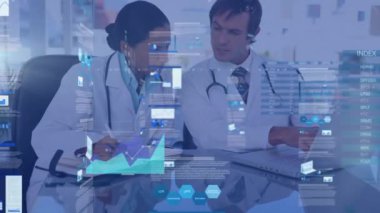 The doctor is using a laptop while his colleague is taking notes in an office. The interface on the laptop is on the alpha channel.