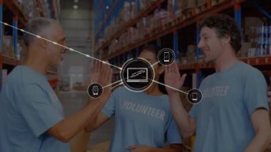 Animation of icons connecting with lines over diverse volunteers giving high five in warehouse. Digital composite, multiple exposure, happy, teamwork, technology, phone, laptop, logistics, shipping.