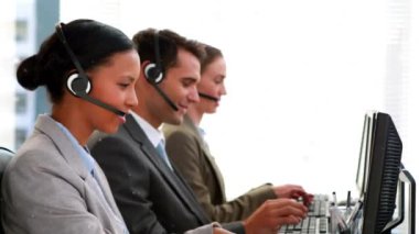 Animation of white particles over team of diverse customer care executives working at office. Business technology concept