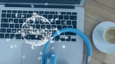 Animation of profile pictures around globe, high angle view of headphone, drink and laptop on table. Digital composite, multiple exposure, globalization, communication and technology concept.