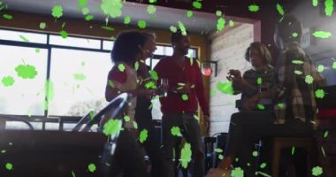 Animation of st patrick's day green shamrock falling over diverse friends having fun at party. St patrick's day, irish tradition and celebration concept digitally generated video