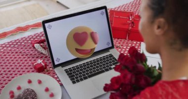 Animation of emoji icon over african american woman using laptop with copy space, slow motion. Valentine's day and love concept digitally generated video.