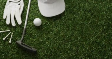 Close up of golf club, ball, glove and peaked cap on grass, copy space, slow motion. Golf, sport and hobby concept.