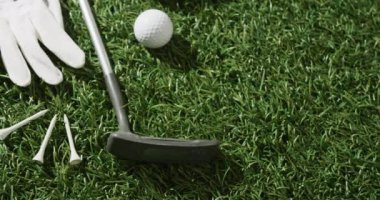 Close up of golf club, ball, glove and peaked cap on grass, copy space, slow motion. Golf, sport and hobby concept.