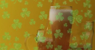 Animation of st patrick's day green shamrock falling over beer glasses. St patrick's day, irish tradition and celebration concept digitally generated video