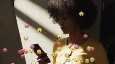 Animation of social media emoji icons over african american woman using smartphone. Global social media, computing and data processing concept digitally generated video.