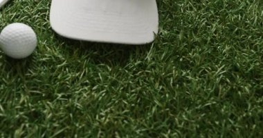 Close up of golf club, ball, glove and peaked cap on grass, copy space, slow motion. Golf, sport and hobby concept.