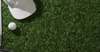 Close up of golf club, ball, glove and peaked cap on grass, copy space, slow motion. Golf, sport and hobby concept.