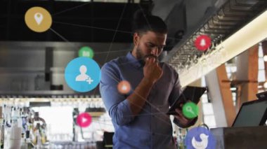 Animation of social media icons with network over biracial businessman using tablet. Global social media, business, finances, computing and data processing concept digitally generated video.