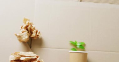 Close up of paper trash and cup with plant on cardboard background, with copy space. Global recycling, ecology and nature concept.