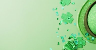 Video of st patrick's green shamrock leaves and hat with copy space on green background. St patrick's day, irish tradition and celebration concept.