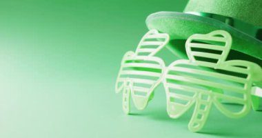 Video of st patrick's shamrock leaf glasses and hat with copy space on green to white background. St patrick's day, irish tradition and celebration concept.