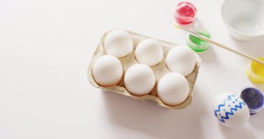 White eggs with colorful paints and brush on white background with copy space. Easter, tradition and celebration concept.