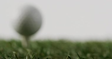 Close up of golf tee and ball on grass and white background, copy space, slow motion. Golf, sport and hobby concept.