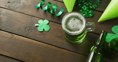 Video of st patrick's green beer, shamrock and bottle on wooden background. St patrick's day, irish tradition and celebration concept.
