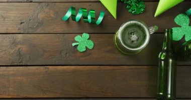 Video of st patrick's green beer, shamrock and bottle on wooden background. St patrick's day, irish tradition and celebration concept.