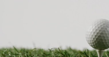 Close up of golf tee and ball on grass and white background, copy space, slow motion. Golf, sport and hobby concept.