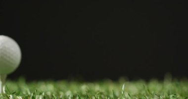 Close up of golf tee and ball on grass and black background, copy space, slow motion. Golf, sport and hobby concept.