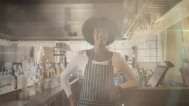 Animation of portrait of african american female shop assistant with apron over light spots. Global business and digital interface concept digitally generated video.