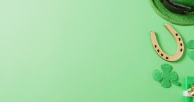 Video of st patrick's green shamrock leaf, horse shoe, hat with copy space on green background. St patrick's day, irish tradition and celebration concept.