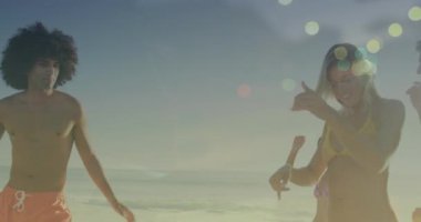 Animation of light spots over happy diverse friends dancing at beach. Friendship and celebration concept digitally generated video.